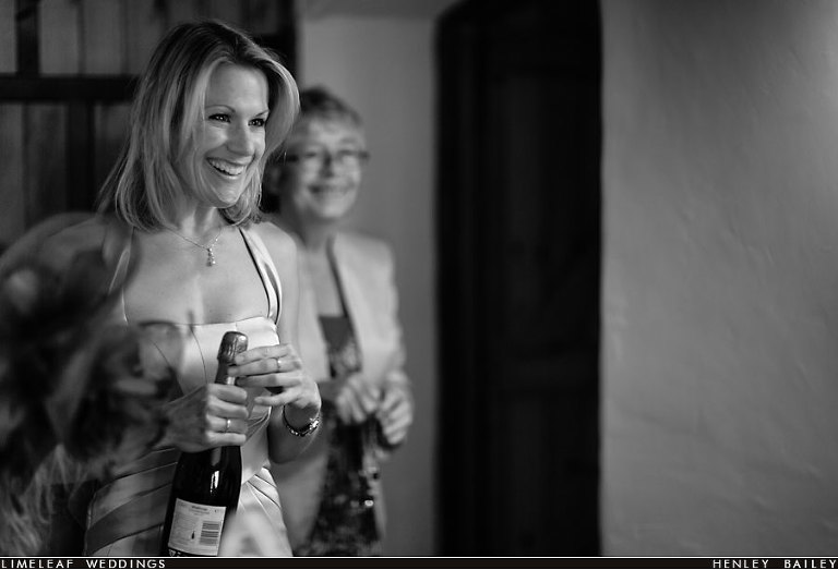 Brides friend smiles while opening bottle of champagne