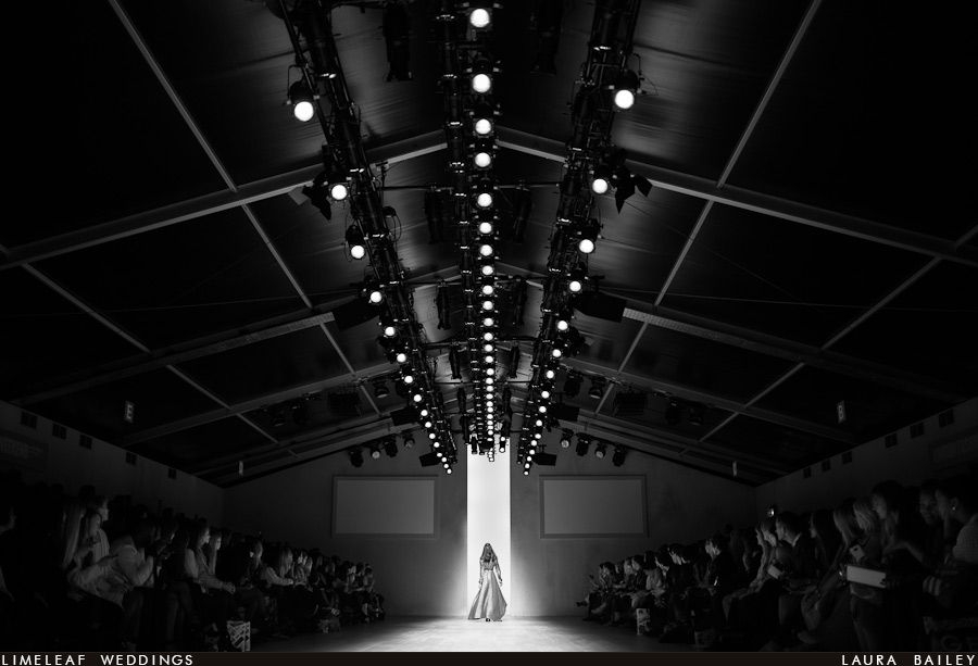 Model in a grey coat heads off the catwalk and into the wings as the audience look on at fashion week