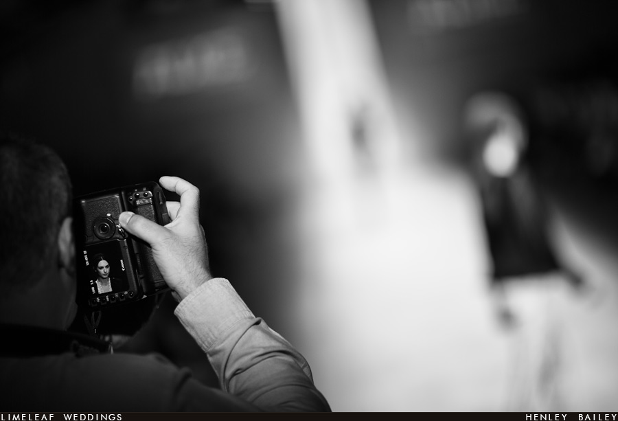 A model is seen heading down the runway in the background while the image of her face is shown on a photographers camera in the foreground