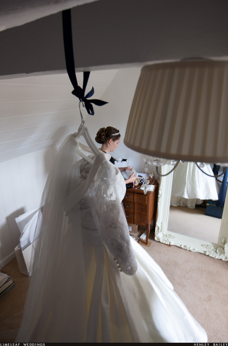 Bride is seen behind her wedding dress which is hanging up in the foreground