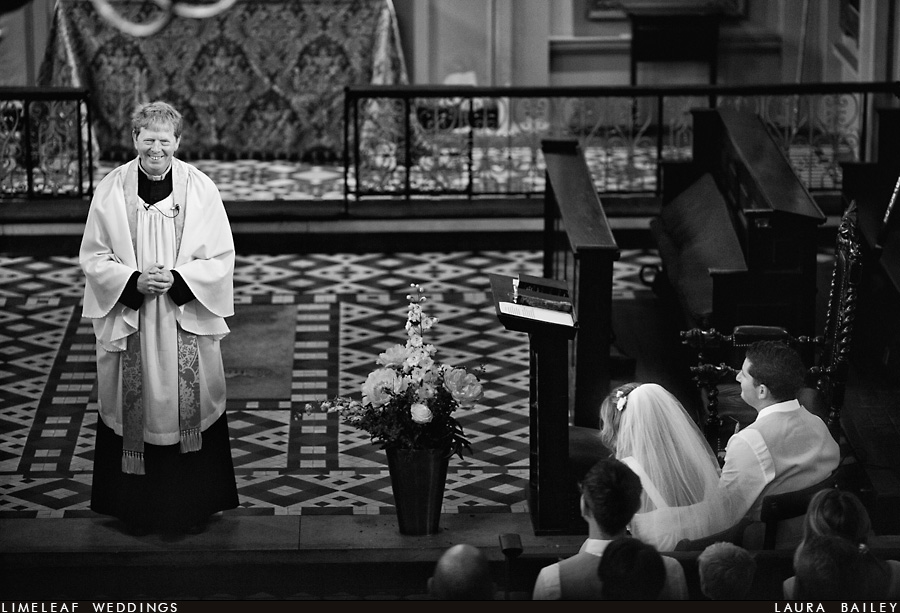 Vicar at St Giles Church smiles during a wedding ceremony as the bride and groom look on